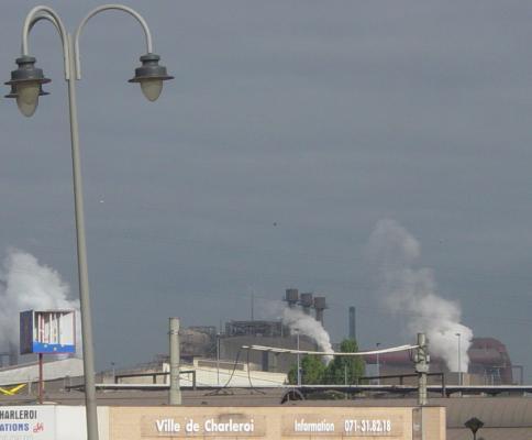 Lampadaire de travers, Charleroi-infos et cheminées industrielles qui fument en face de la gare de Charleroi-Sud
