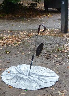 Photo d'un parapluie retourné sur le sol, au manche duquel est accroché un disque