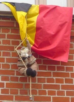 Photo d'un père Noël en peluche escaladant un mur (en plein été, le rouge a déteint), entortillé dans un drapeau belge.