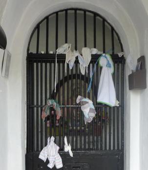 Photo d'une chapelle où sont noués des vêtements de bébés sur la grille